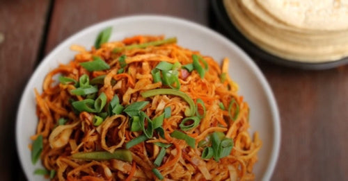 A plate of noodles with green onions and tortillas