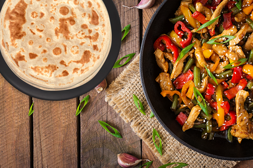 A pan with fried vegetables next to a flatbread
