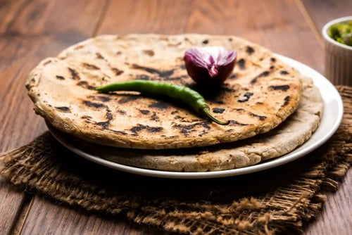 Jowar roti placed on a plate on wooden table with half onion and a green chilli on roti
