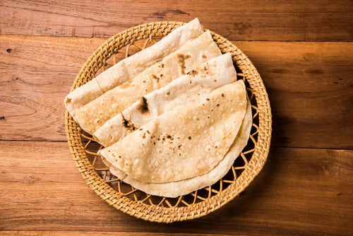 A wooden basket full of wheat roti on a table