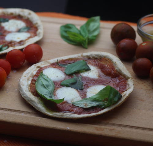 Two pizzas with tomatoes and basil on a wooden cutting board